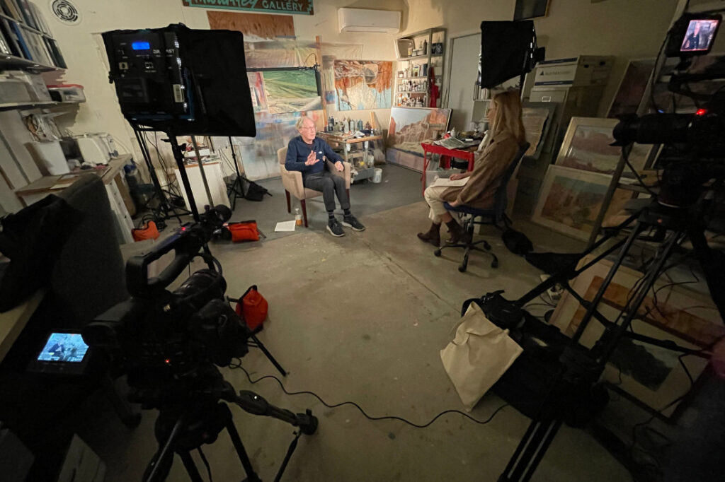 An interview with an artist in his vibrant studio filled with colorful artwork and art supplies.