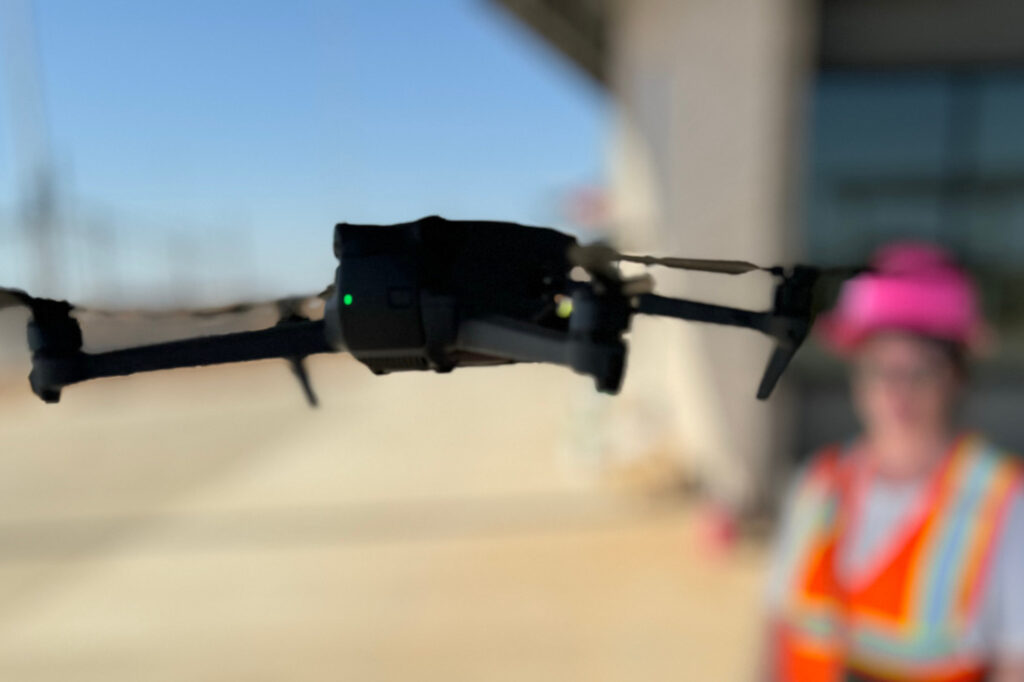 Drone flying in the foreground at a construction site in Queen Creek, with the company founder wearing safety gear in the background.